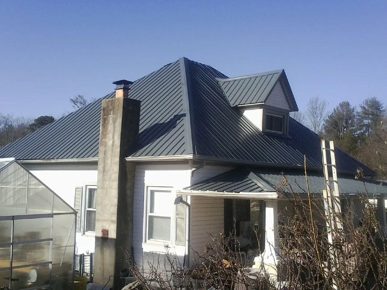 Dark blue standing seam metal roof on a white farmhouse with dormer — Slate & Tile Roof Repair by Roofing Brothers in Clifton