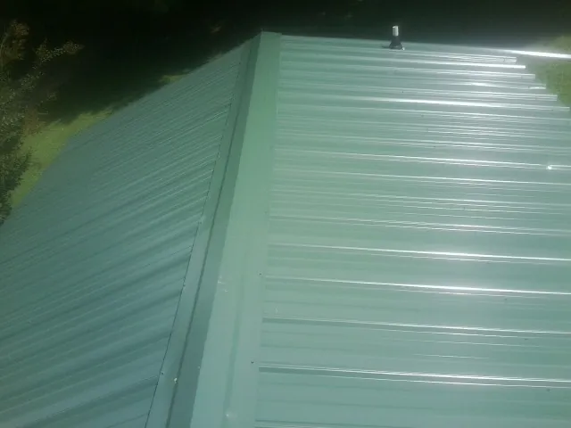 New green metal panels meeting at the ridge of a roof — Flat Roof Repair work by our crew in Clifton